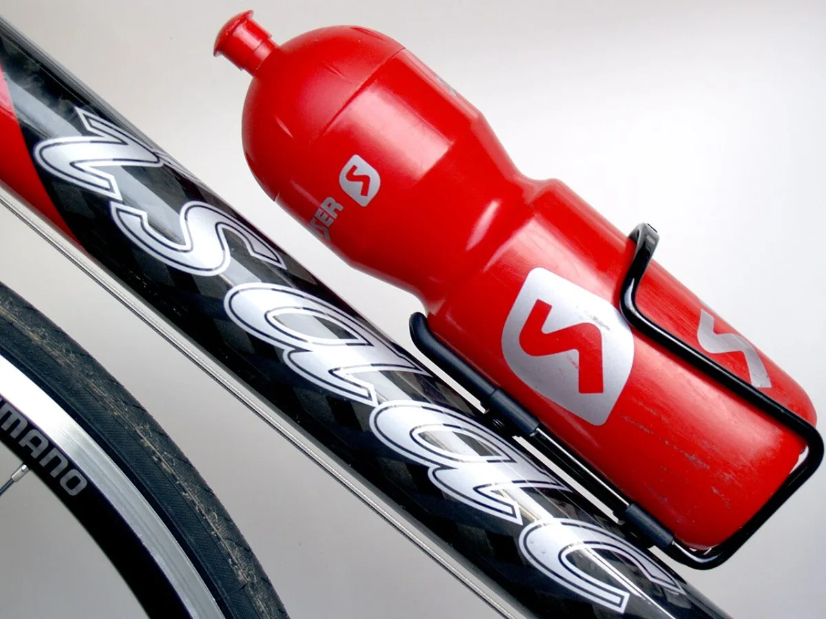 Rode drinkfles in een bidonhouder bevestigd aan het frame van een racefiets
